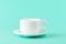Empty porcelain coffee cup and a saucer over a mint green color background. White ceramic teacup. Modern stylish tableware. Copy s