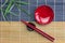 Empty red bowl with red chopsticks on holder and bamboo leaves placed on bamboo mat