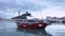 Empty red fishing motorboat with inflatable false killer whale on roof tent moored at city port under cloudy sky in calm