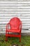 Empty red metal chair next to abandoned old building