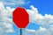 An empty red shield stop shield against a blue sky with clouds