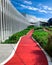 Empty red walkway for running in the garden near shopping mall. Running track in the park with green ornamental plant on sunny day