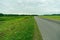 An empty roadway outside the city passes by agricultural fields. A highway with a new asphalt surface on the background of fluffy