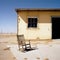 An empty rocking chair on a porch overlooking a boarded up factory and a barren landscape its owner nowhere to be seen