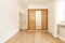 Empty room with a built-in wardrobe with sliding mirror doors combined with wood and a white wooden door and laminated flooring