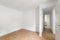 Empty room with laminate flooring and newly painted white wall in refurbished apartment with corridor leading to