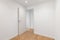 Empty room with laminate flooring and newly painted white wall in refurbished apartment with corridor leading to other