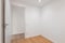 Empty room with laminate flooring and newly painted white wall in refurbished apartment with corridor leading to other