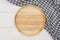 Empty round wooden plate with grey gingham tablecloth on white wooden table.