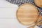 Empty round wooden plate with spoon, fork and grey gingham tablecloth on white wooden table.