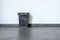 Empty rubbish basket on black floor and white wall behind