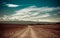 Empty rural road going through prairie under cloudy sky