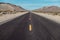 Empty scenic long straight desert road with yellow marking lines.