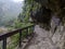 Empty Shakadang Trail with warning signs on the wall along cliffs and trees with Liwu River in a mist during the