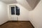 Empty small room with wooden oak parquet floor, newly painted white walls, heating radiator and a window. Attic room