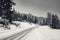 Empty snowcapped road with car tracks in dramatic black and white foggy landscape mountain range in dolomites in wintertime, giau