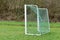 Empty soccer goal with white frame and green net standing on grass at forest playground