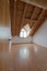 Empty spacious and bright room in a refurbished apartment with wooden parquet floor and white walls and slanted wooden ceiling wit