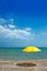 An empty sunny sandy sea beach with a yellow umbrella