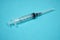 Empty syringe with needle on a turquoise background.