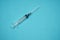 Empty syringe with needle on a turquoise background.