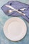 Empty table setting arrangement, white plate, cutlery, blue napkin, concrete table surface, flatlay