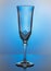 Empty transparent champagne glass on a thin high leg in light blue gradient backlight on a glossy surface