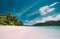 Empty tropical secluded sandy beach with coconut palm trees against a blue sky with white clouds