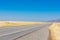 Empty two way road navigates between scenic agriculture fields toward hills under blue sky