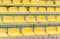 Empty vacant stadium stands, chairs, yellow plastic arena spectator seats, detail, small football soccer field, daytime, closeup