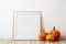 An empty vertical wooden frame for mockup stands near the jack o lantern pumpkins. White wall background. Halloween decor