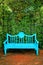 Empty vibrant turquoise blue wooden bench on terracotta brick path in green garden