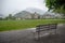 Empty wet metal bench in front of a green field at Interlaken with foggy mountain and buildings background