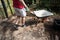 Empty wheel barrow being help in a garden yard by a man with his legs showing.