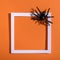 Empty white frame with scary black spider on orange paper. Halloween background layout.