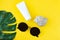 Empty white jar for cream, glasses, seashell and green leaf of monstera on a yellow background. Sun protection concept on the