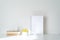 Empty white picture frame mockup in sunlight. Books, coffee cup and sphere-shaped vase with small yellow flowers. Concept of