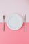 Empty white plate with cutlery on a pink-peach background.