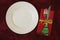 Empty white plate with fork and knife on a red fabric napkin with a gold ribbon and fir on a red tablecloth Holiday concept,