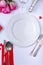 Empty white plate surrounded by pink roses with bottle and cutlery on table