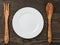 Empty white plate with wood fork and spoon on oak table