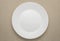 Empty white plate on woven napkin. Clean plate on light brown tablecloth. Unused dishes.