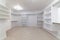 Empty white shelves in a fitted walk-in wardrobe