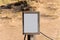 Empty white sign with partly broken wooden frame on a sandy beach