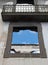 Empty window frames in a roofless abandoned house with a balcony and white interior walls against a blue sky