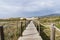 Empty, wooden boardwalk on a beach Praia do Guincho in Sintra. View of grass and sand with hills and Atlantic Ocean in the