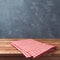 Empty wooden deck table with red cheched tablecloth over blackboard background for product montage display.