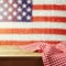Empty wooden deck table with tablecloth over USA flag bokeh background. 4th of July celebration picnic background.