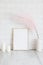 Empty wooden picture frame mockup, candles, pink dried flowers in vase on table. White tiles wall background. Minimal, elegant,