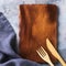 Empty wooden stand, cutlery and napkin with copy space, top view. Food background